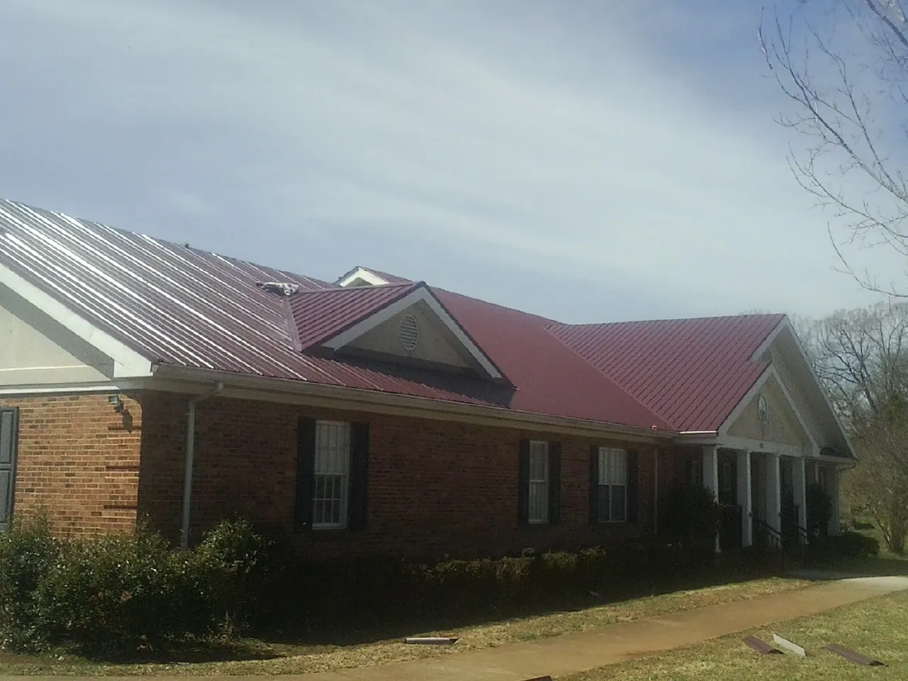Red metal roof with gabled entries on a long brick building, from a Hail Damage Roof Repair job in Pierceton