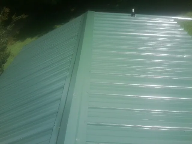 New green metal panels meeting at the ridge of a roof — Flat Roof Repair work by our crew in Pierceton