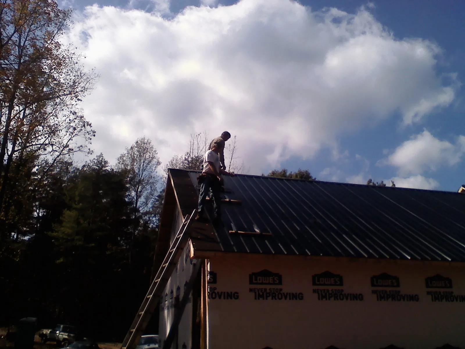 Roofer fastening dark metal panels high against a cloudy sky, from a Roof Inspection job in Pierceton