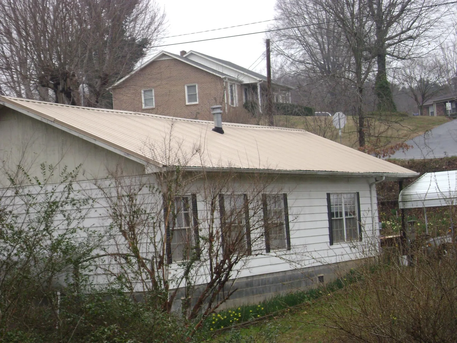 Tan metal roof on a white sided house set into a hillside — Commercial Roofing by Roofing Brothers in Pierceton