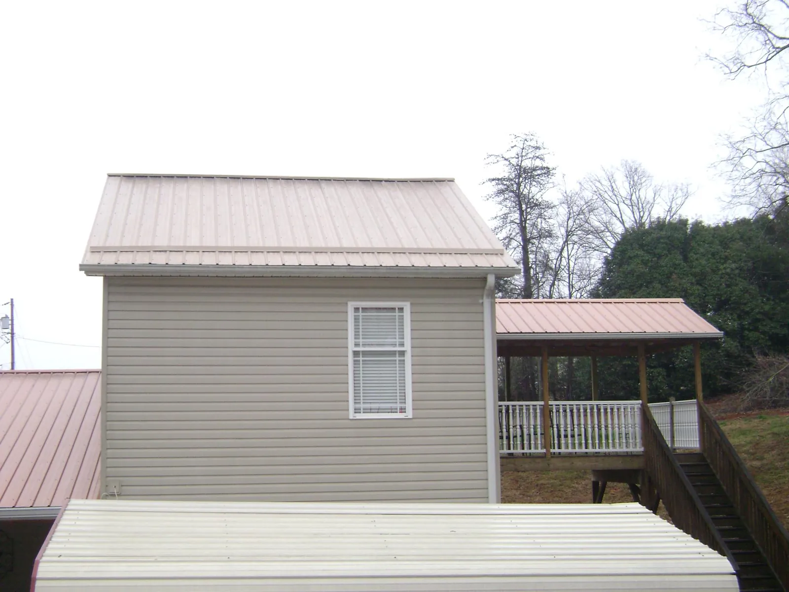 Tan metal roofs on a two story addition and attached porch, from a Roof Replacement job in Pierceton